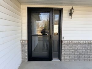 A black front door with a glass storm door, next to a window, set in a house with white siding and light brick trim.